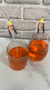 Two glasses of orange liquid with novelty straws featuring faces on a marble surface.